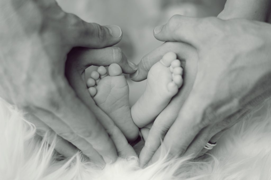 grayscale-photo-of-baby-feet-with-father-and-mother-hands-in