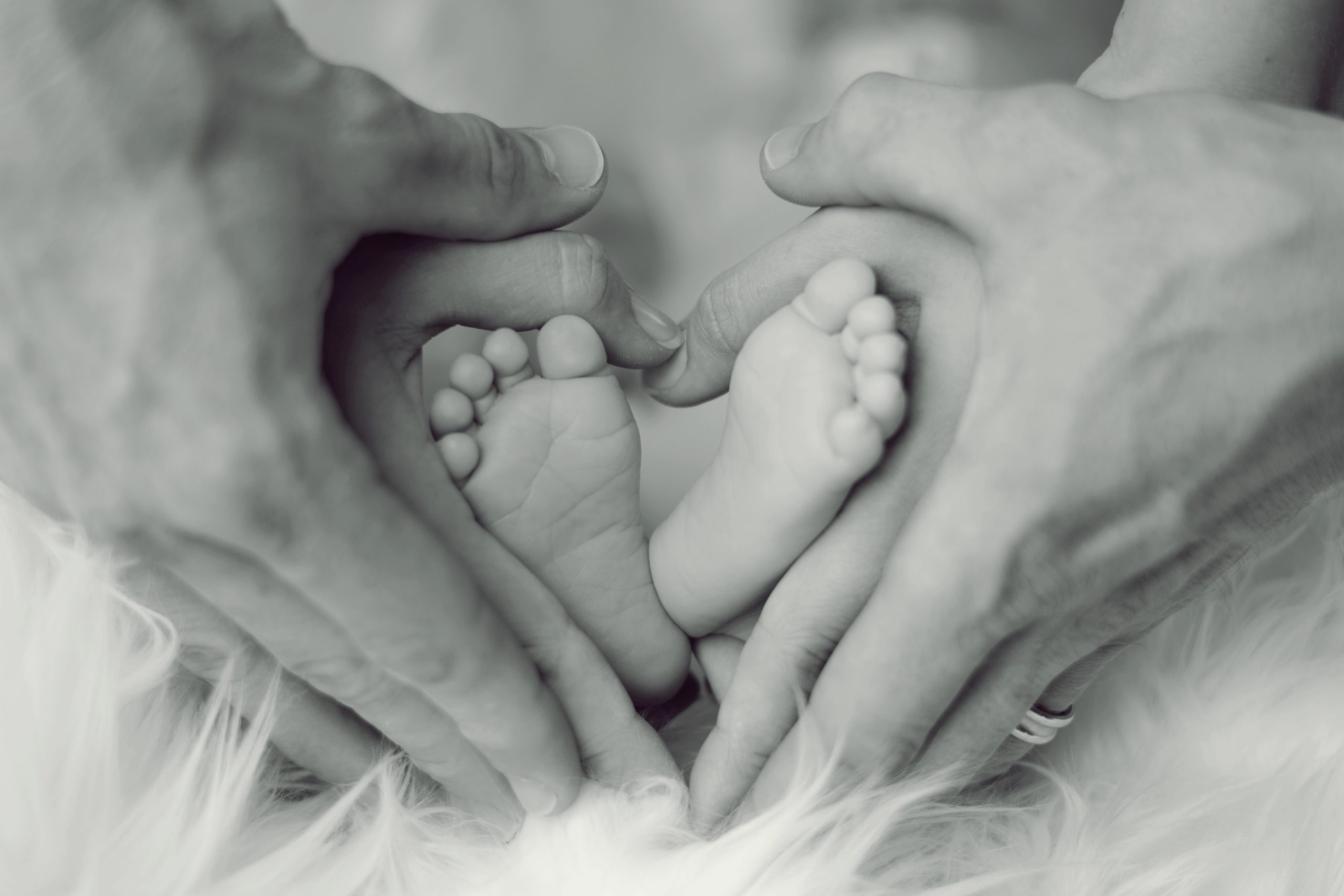 grayscale-photo-of-baby-feet-with-father-and-mother-hands-in