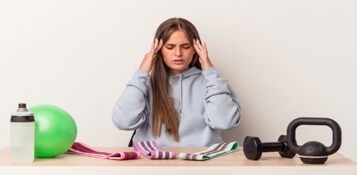 young-caucasian-woman-sitting-table-with-sport-equipment-isolated-white-background-touching-temp