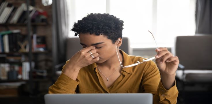 young-woman-sitting-at-work-desk-holding-her-head