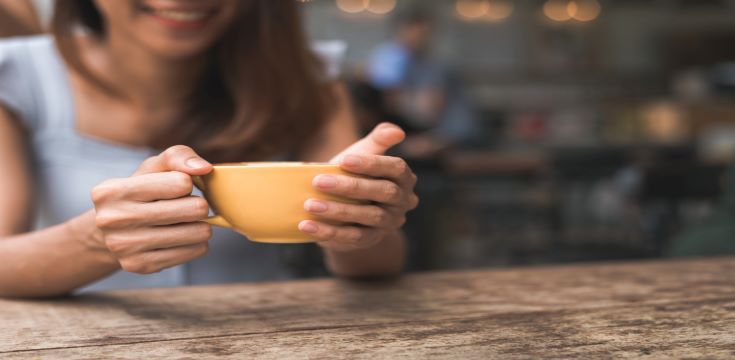 cheerful-asian-young-woman-drinking-warm-coffee-tea-enjoying-it-while-sitting-cafe