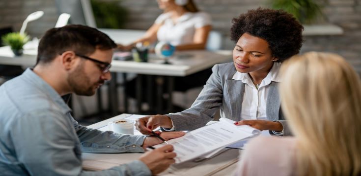 black-female-real-estate-agent-showing-couple-where-sign-contract-during-meeting-office