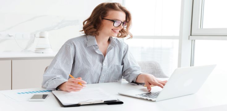 happy-brunette-businesswoman-glasses-using-laptop-computer-while-working-light-apartment