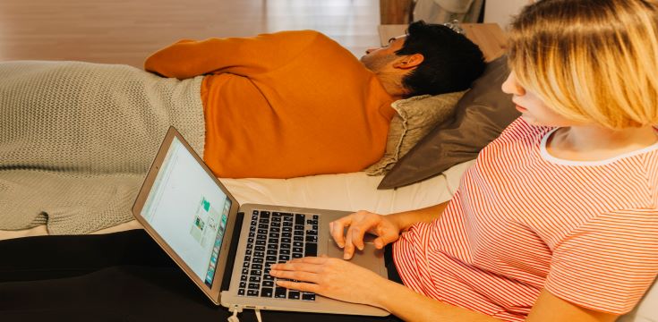 pretty-woman-browsing-laptop-near-sleeping-man