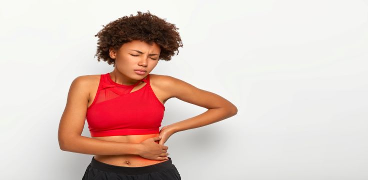 dissatisfied-woman-holds-aching-hip-has-kidney-inflammation-touches-location-pain-near-ribs-marked-with-red-dot-wears-sport-bra