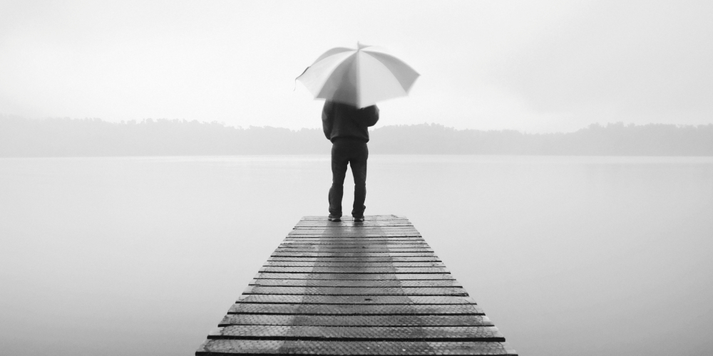 man-holding-umbrella-jetty-by-tranquil-lake