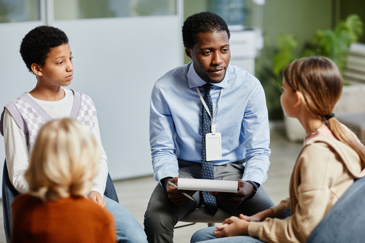 Portrait of young African-American psychologist listening to children in support group circle