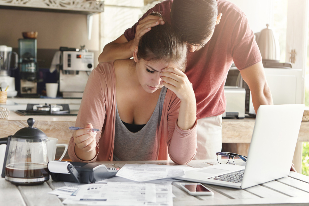 unhappy-couple-unable-pay-loan-time-stressed-female-doing-paperwork-sitting-table-with-laptop-papers-calculator-cell-phone-man-trying-support-his-wife